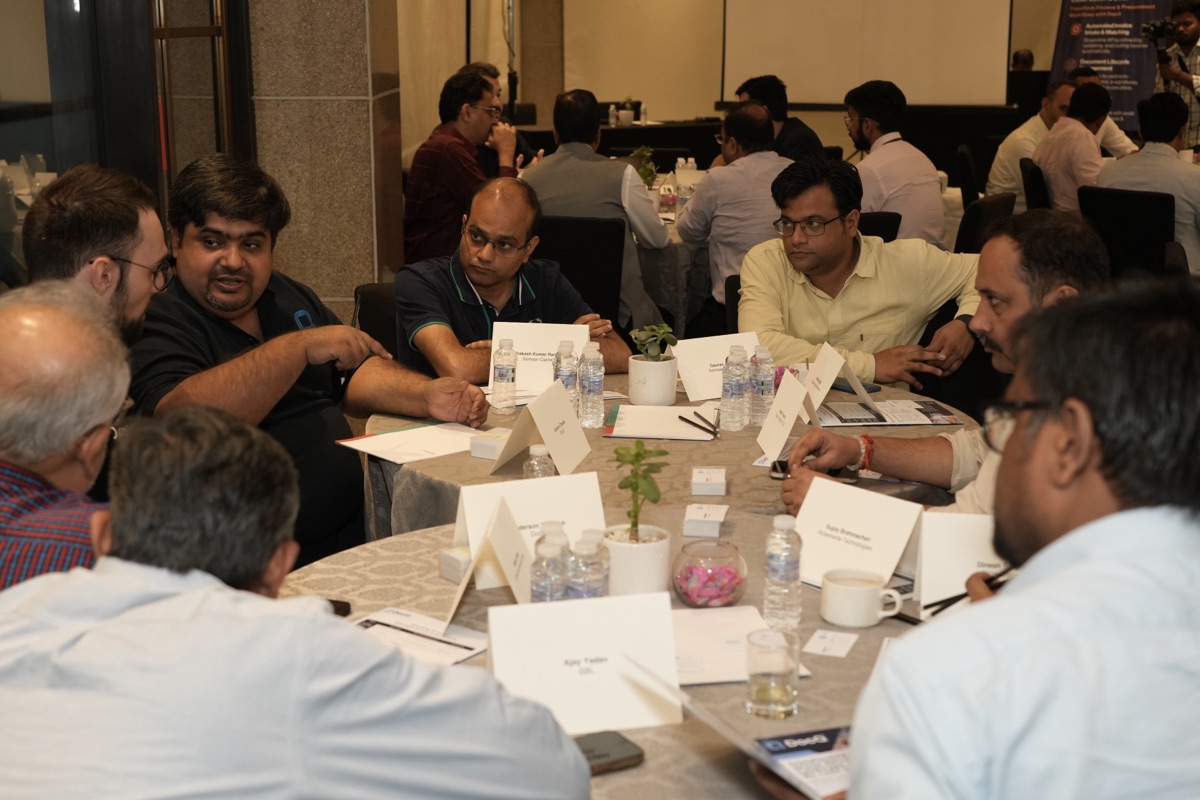 Close-up of table discussion with attendees exchanging ideas, DocQ presentation visible in background